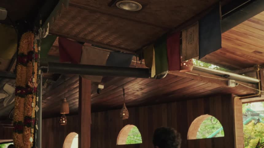 Tibetan prayer flags and a marigold garland sway gently from the ceiling of a tranquil, wooden interior
