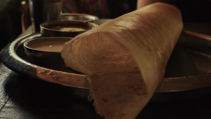 A close-up dolly shot reveals a delicious Indian Dosa served on a metal plate with chutney and sambar