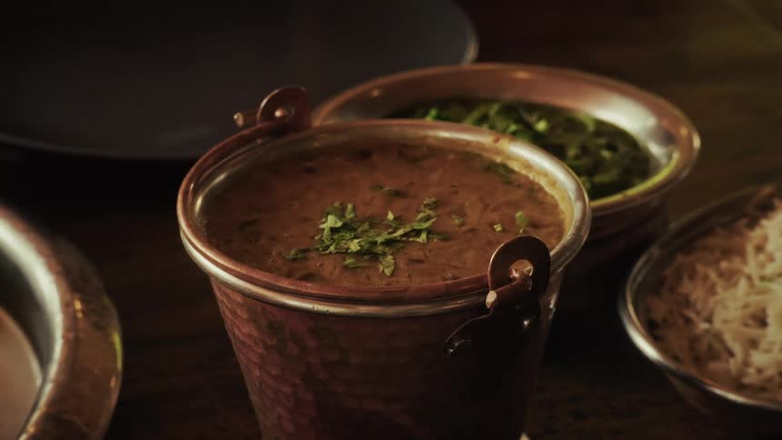 A slow pan reveals authentic Indian cuisine, including lentil curry and rice, served in traditional copper bowls