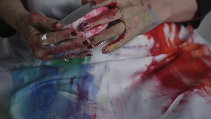 Woman with paint covered hands holds a paint covered mug