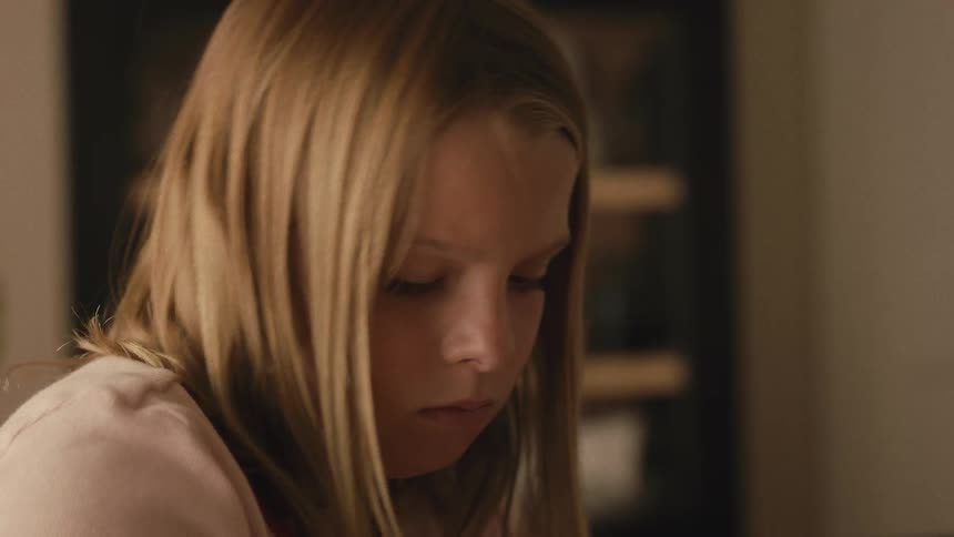 A young girl with blonde hair is deeply focused on her artwork, carefully drawing with a pencil
