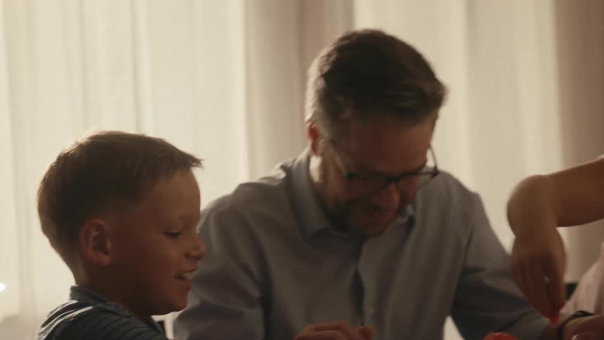 A father and his two children happily conduct a red volcano science experiment together at their dining room table