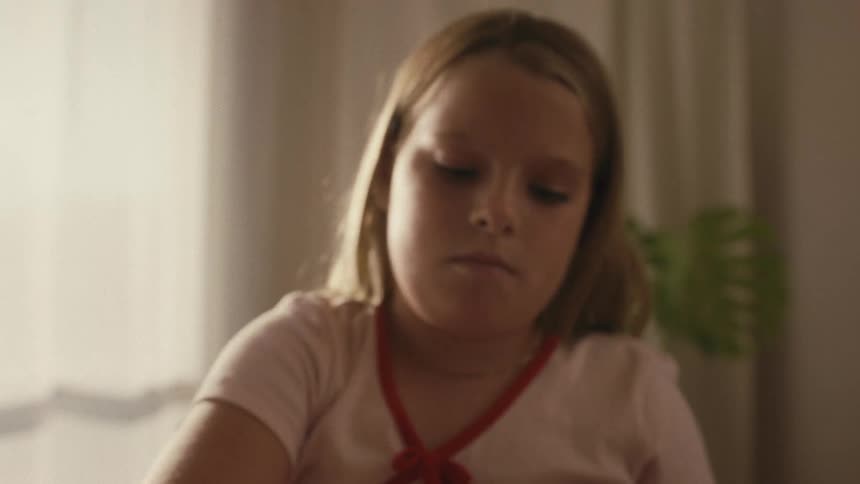 A young blonde girl concentrates as she uncaps a yellow marker and begins to draw in her room