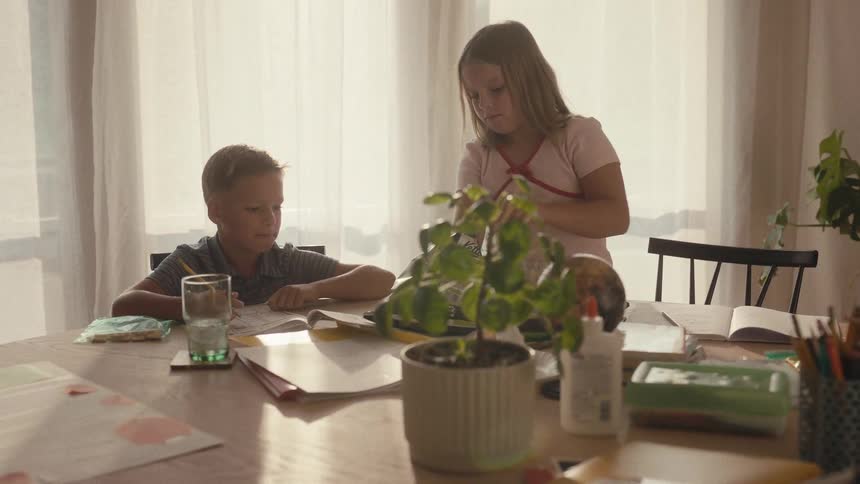 A young girl joins her brother at the dining room table to do homework and share a snack in their sunlit home