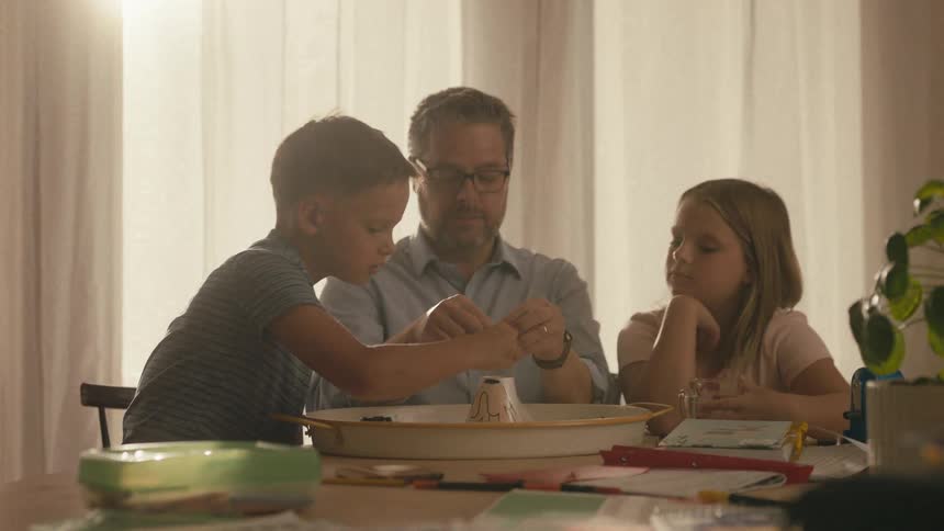 A father and his two kids do a fun volcano science experiment together at home during golden hour