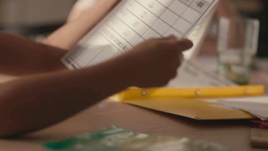 A young boy with a serious expression diligently focuses on completing his homework at a table