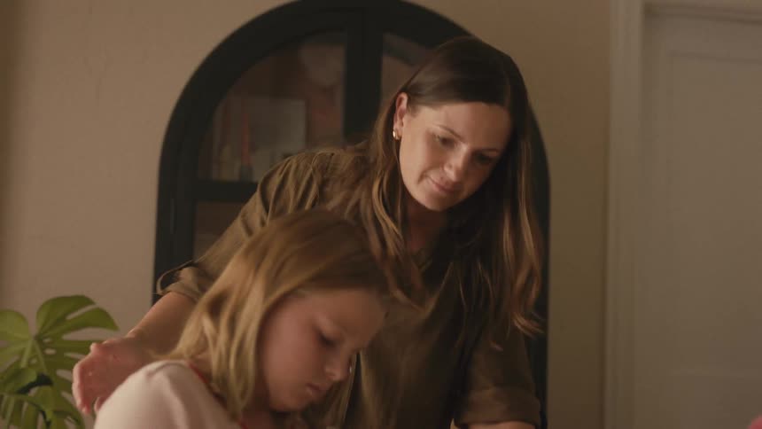 A loving mother watches her young daughter color a picture at their home dining table