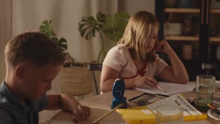 A young brother and sister study quietly together at the dining table, becoming tired as they do their homework