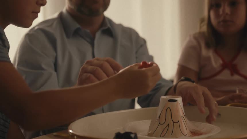 A father helps his son and daughter with a homemade volcano science project in slow motion