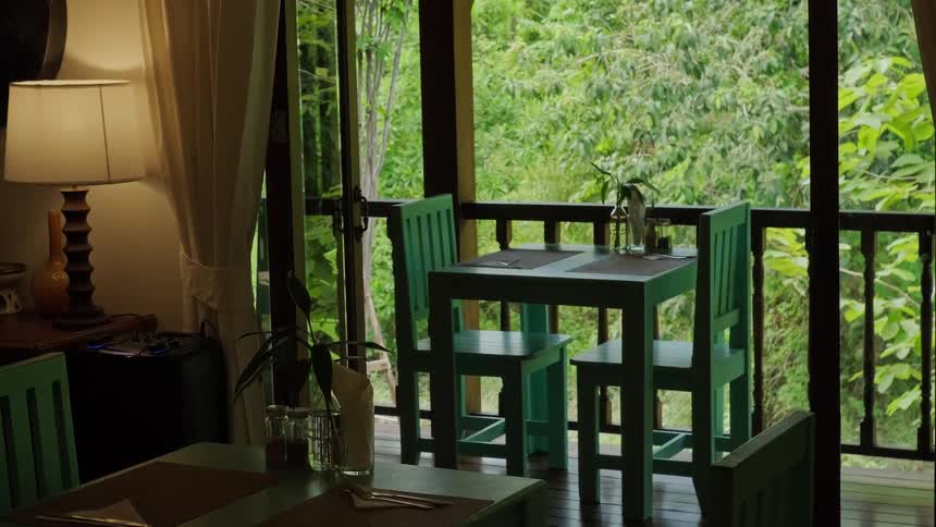 An empty table for two sits on a tranquil restaurant balcony overlooking a lush, green tropical forest