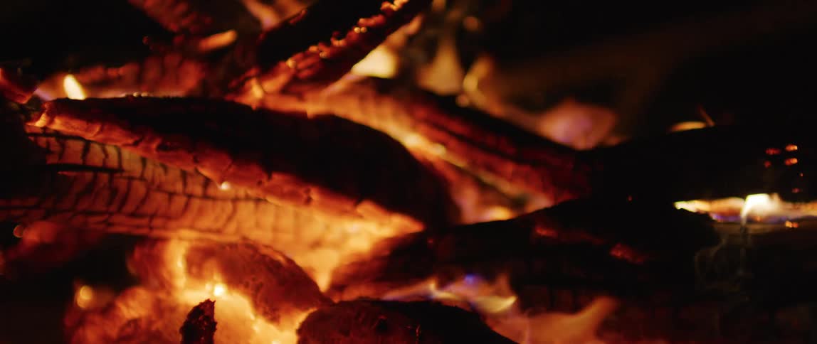 A mesmerizing close-up of a cozy campfire with glowing embers and slow-motion flames flickering in the dark