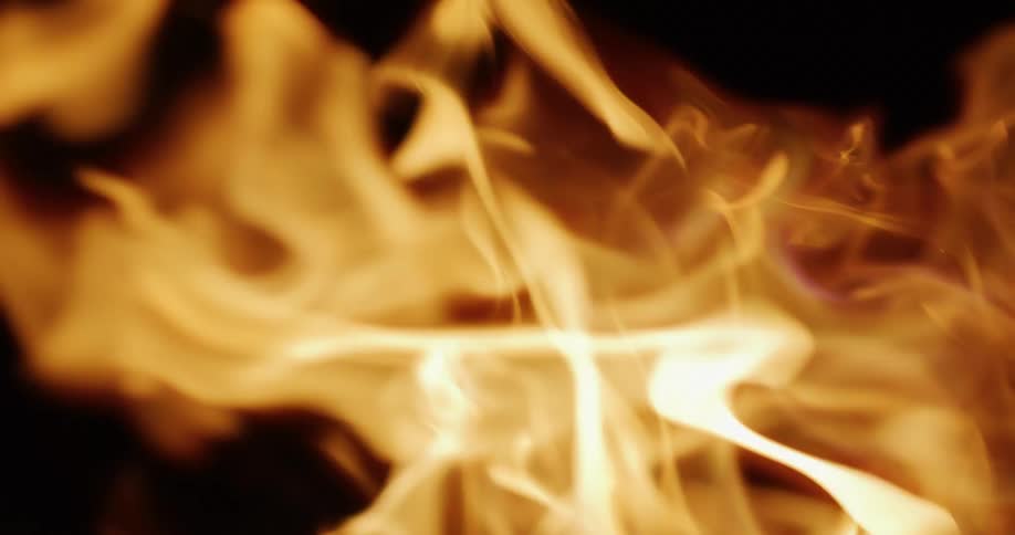 Extreme close-up of a log burning in a fireplace with warm flames licking up into the darkness