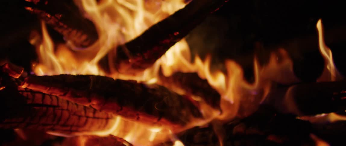 A mesmerizing close-up of a warm campfire with burning logs and flickering flames in slow motion