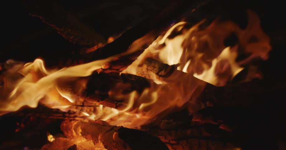A mesmerizing close-up of a warm campfire with flames dancing over glowing logs in slow motion