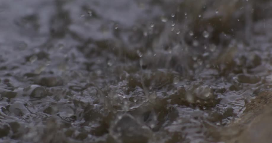 An extreme close-up in super slow motion of heavy raindrops splashing into a muddy puddle