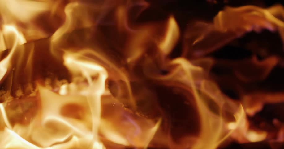 A mesmerizing slow-motion closeup of a warm, crackling fire with glowing embers and vibrant orange flames