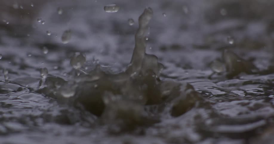 A close-up, slow-motion shot of raindrops creating dramatic splashes and ripples in a murky puddle of water