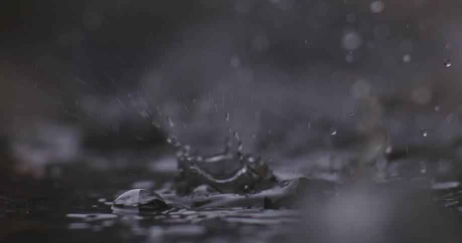 A super slow-motion close-up of raindrops falling and splashing into a dark puddle