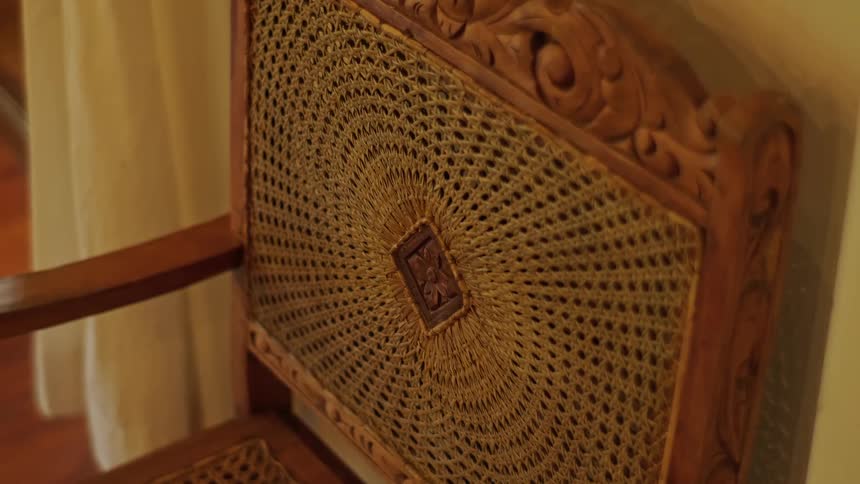A close-up shot of an ornate, hand-carved antique wooden chair with an intricately woven wicker backrest