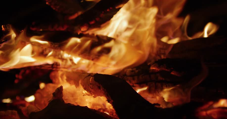 A slow-motion close-up captures the vibrant, dancing flames and glowing embers of a warm, crackling campfire