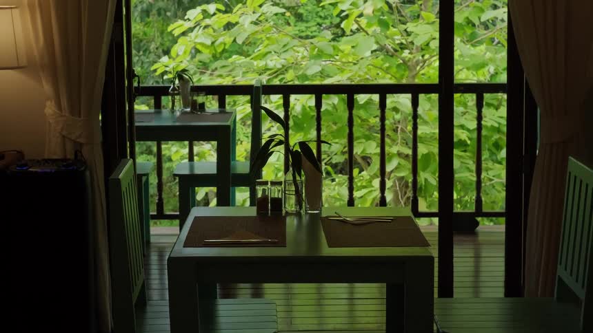 A peaceful view from a dining room onto a balcony overlooking a vibrant, green tropical jungle