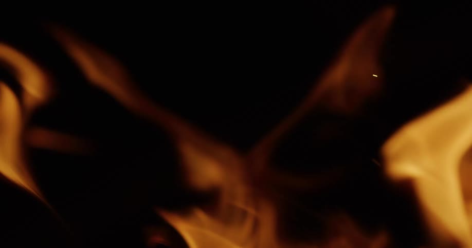 A close-up, slow-motion shot shows golden orange flames dancing and flickering against a black background