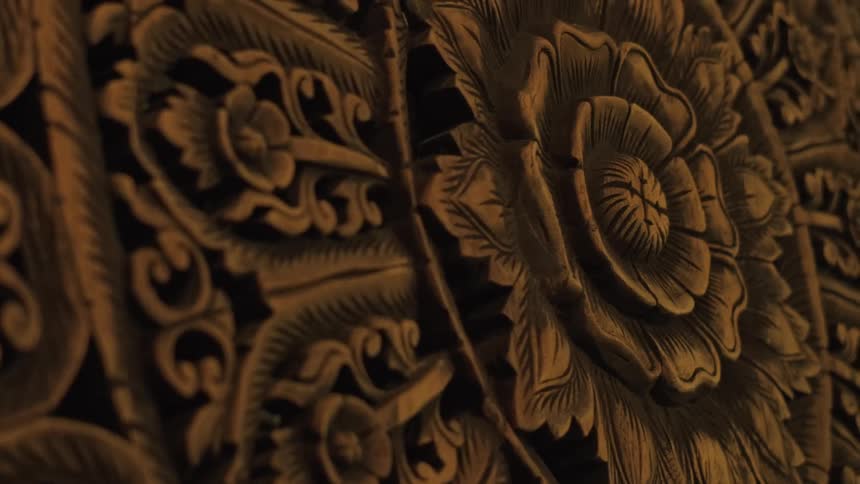 A slow-panning close-up shot of an intricate, traditional floral pattern carved into wood