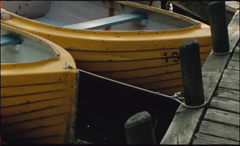 Two yellow rowboats are tied to a rustic wooden dock, gently bobbing in the calm water