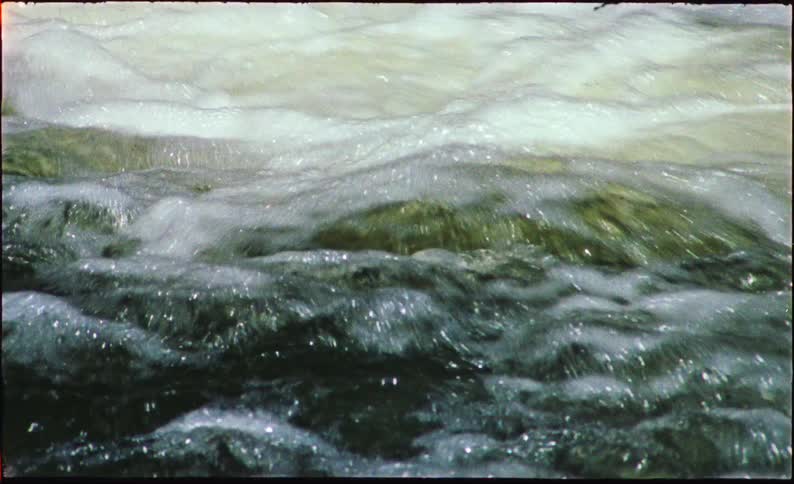 Close-up film shot captures the turbulent, foamy surface of fast-moving river rapids