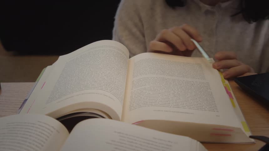 A student slowly turns the page of a book while studying, then begins typing on a laptop