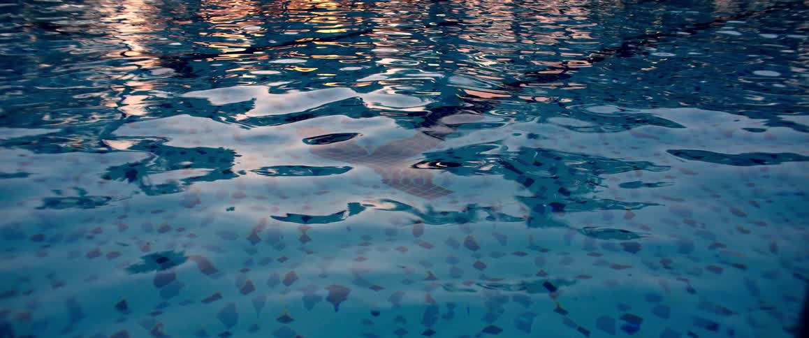 Close-up of a tranquil swimming pool at dusk, with the water surface reflecting the golden sunset