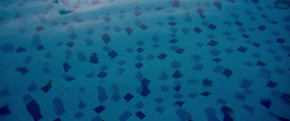 Golden light from a sunset reflects off the serene, rippling surface of a blue tiled swimming pool in slow motion