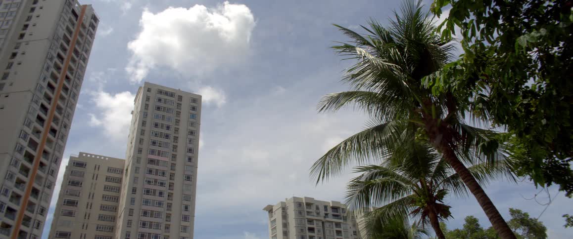 A low-angle view of white high-rise buildings and swaying palm trees against a partly cloudy sky