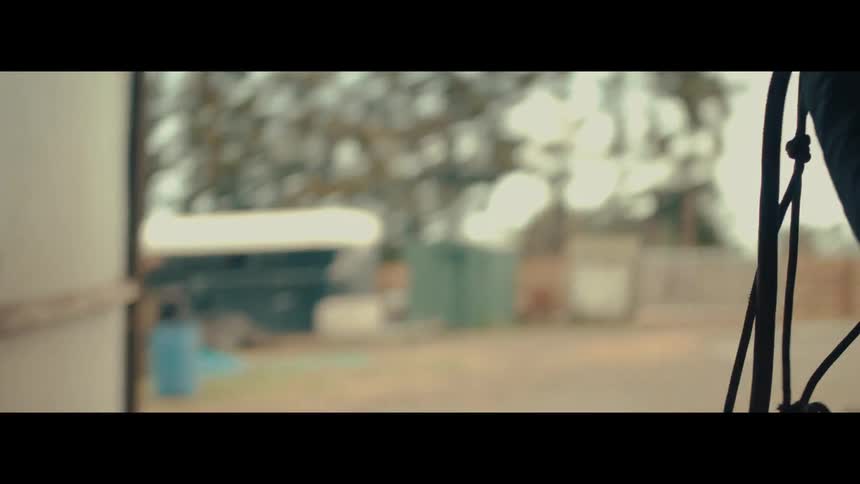 A woman in silhouette grabs a horse bridle and walks out of a dark stable in slow motion