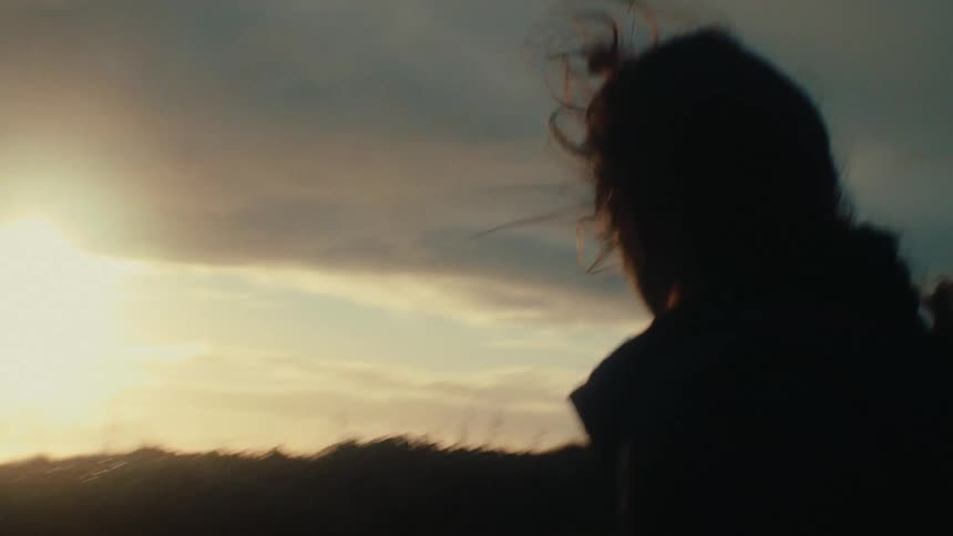 A woman with her hair blowing in the wind is silhouetted as she walks away into the sunset