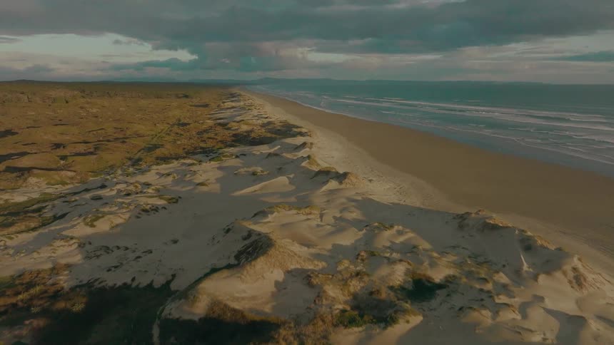 A stunning aerial view captures the golden light of sunset casting long shadows over the sand dunes of a vast, remote coastline
