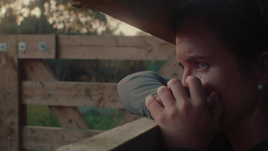Close up shot of a sad and pensive woman with teary eyes leaning against a wooden fence in the countryside