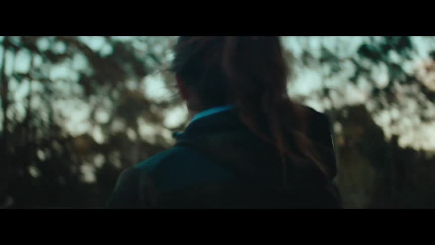 A cinematic slow-motion tracking shot follows a woman as she walks through the countryside at golden hour