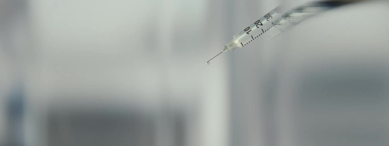 A macro focus pull on a syringe needle tip with a single droplet of medicine ready for injection