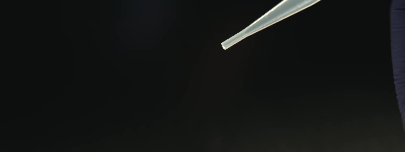 Slow-motion macro shot of liquid droplets falling from a laboratory pipette against a black background