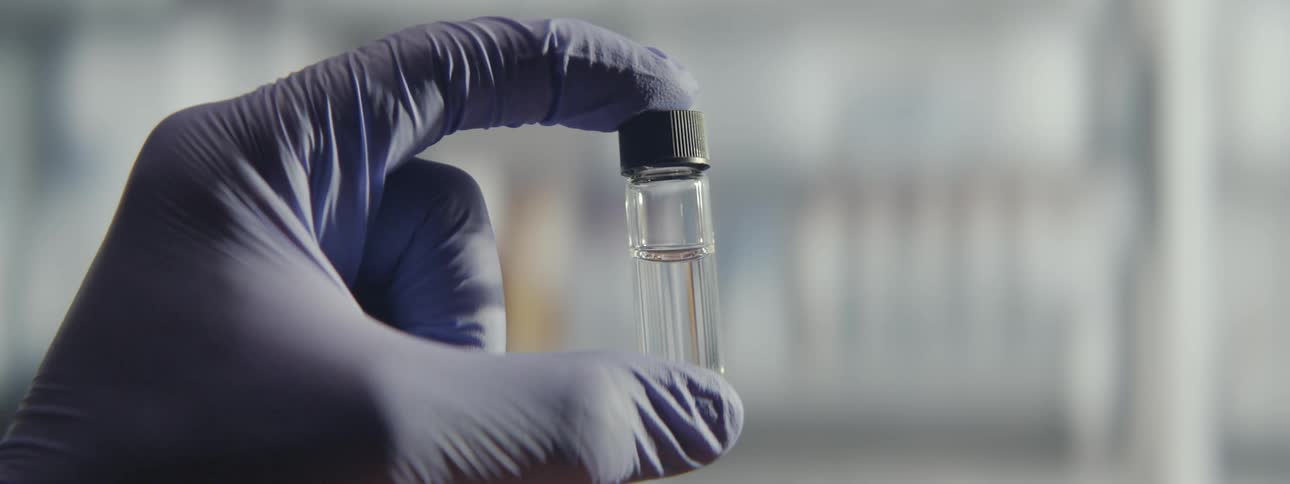 Close-up of a gloved hand holding a vial with a clear liquid in a scientific laboratory