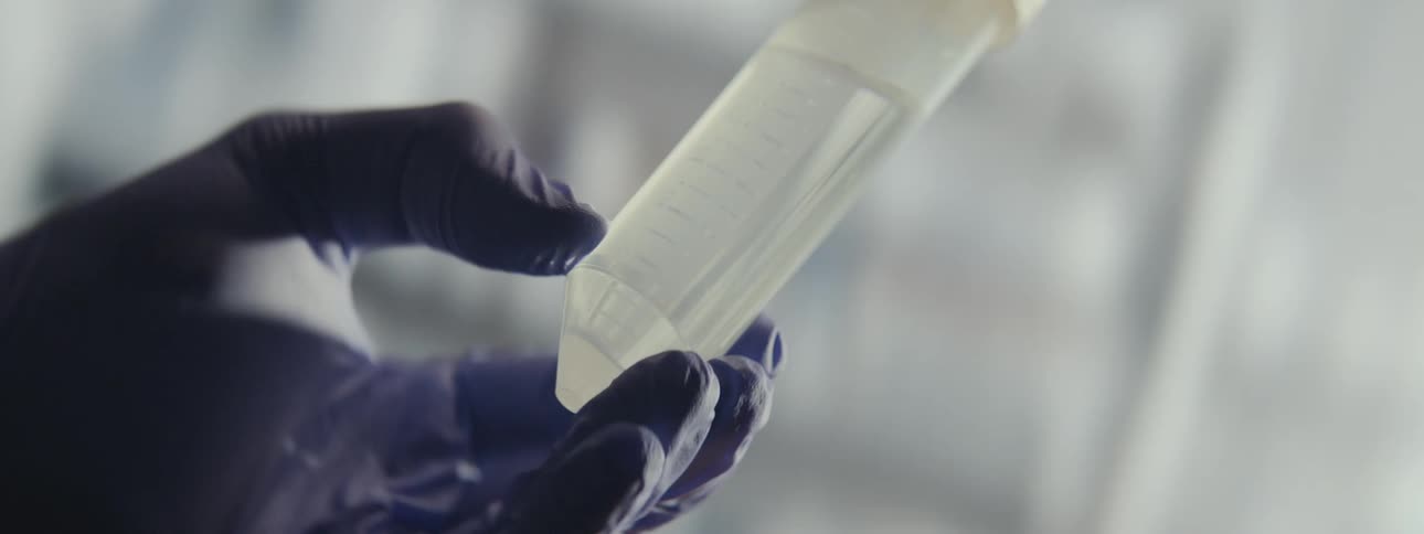 A scientist in a lab carefully agitates a liquid sample inside a plastic conical test tube