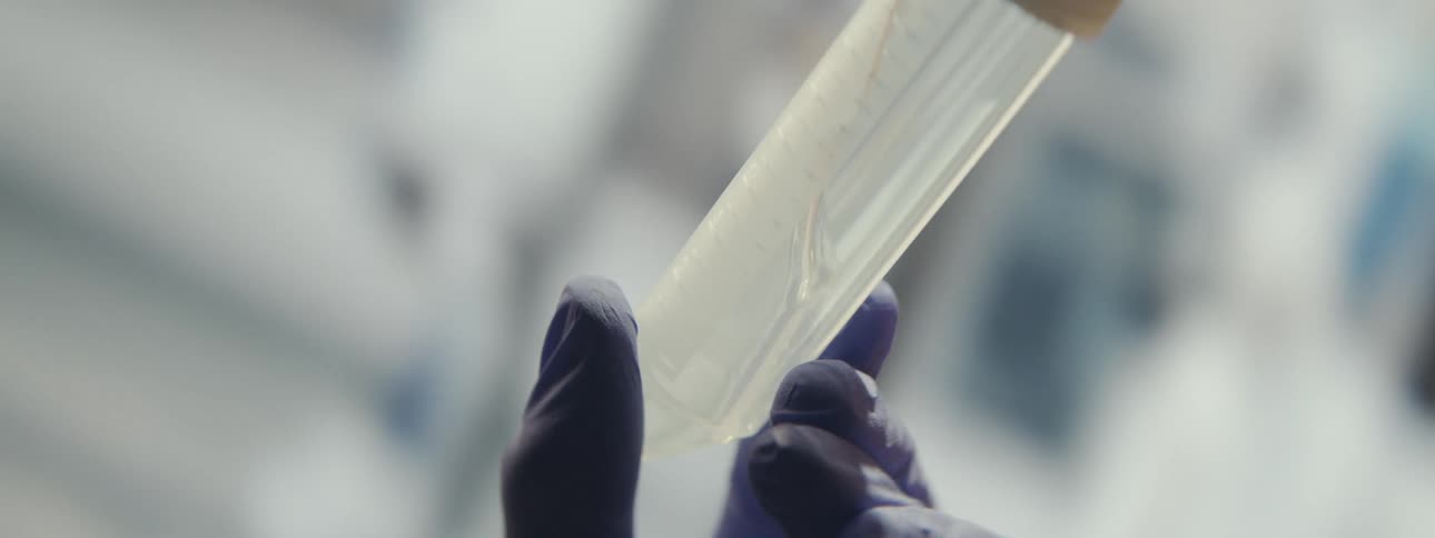 A scientist in sterile gloves examines a liquid sample swirling inside a test tube in slow motion