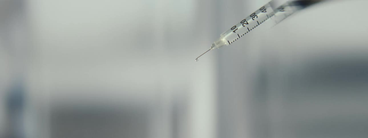 Close-up shot of a syringe spraying a fine mist of clear liquid from the needle tip
