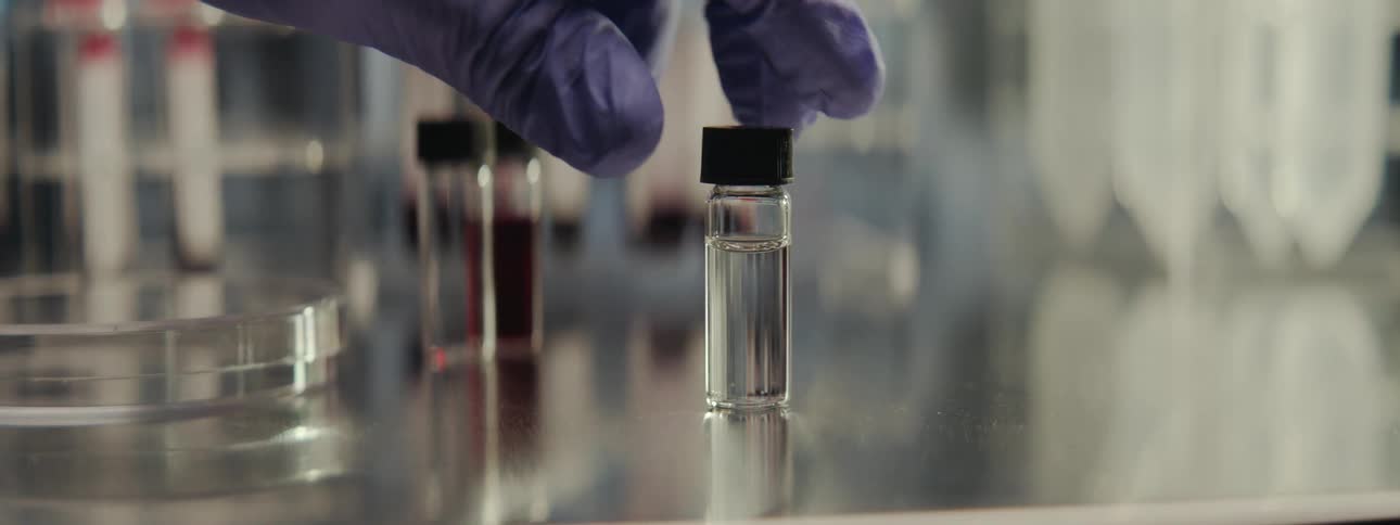 A scientist's gloved hand carefully picks up a vial of clear liquid in a modern laboratory