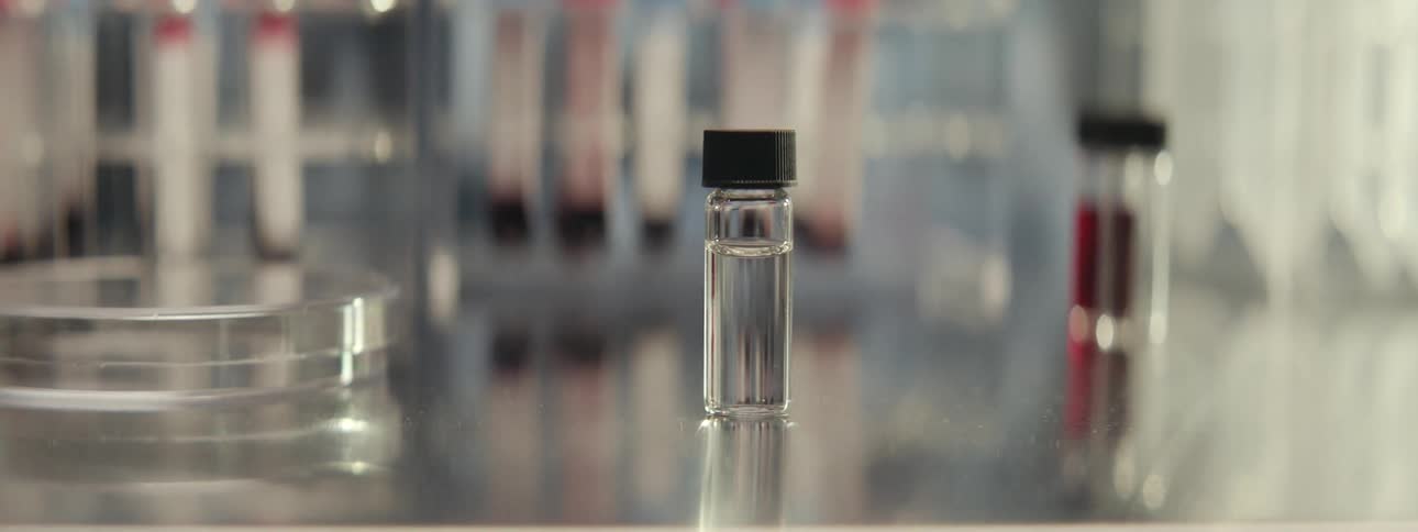 A close-up shot of a small vial containing a clear liquid in a scientific laboratory, with vapor slowly drifting past