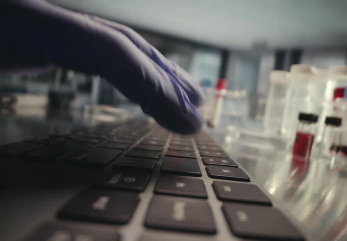Extreme close-up of a scientist in blue gloves typing on a laptop keyboard in a modern research laboratory