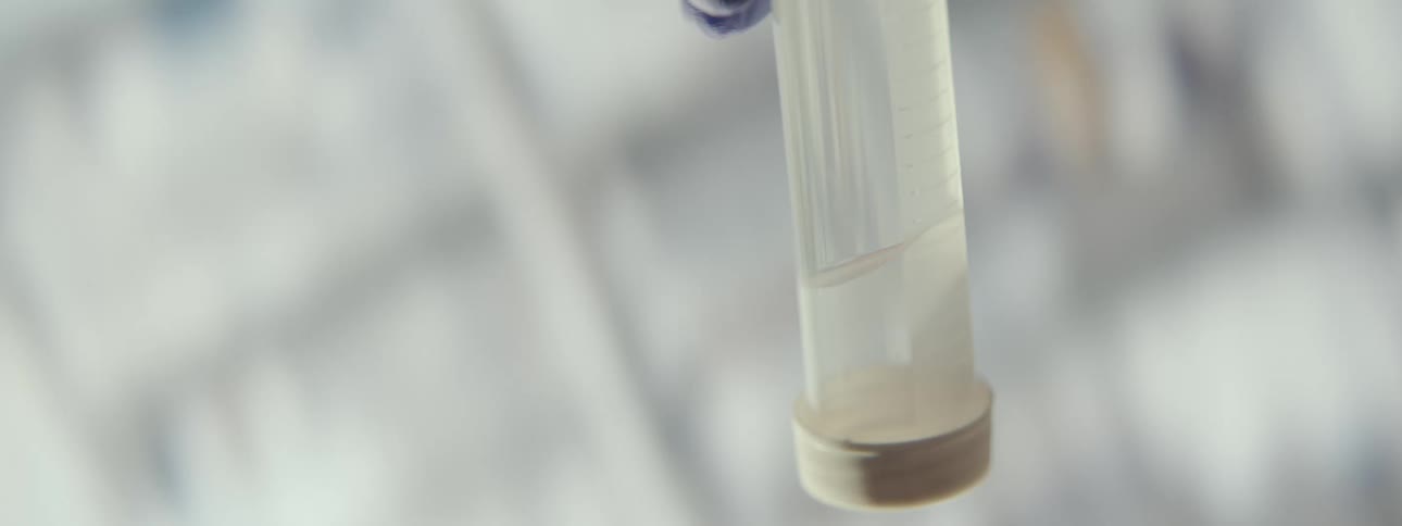 A scientist in a sterile laboratory carefully examines a biological specimen by swirling it in a liquid-filled test tube