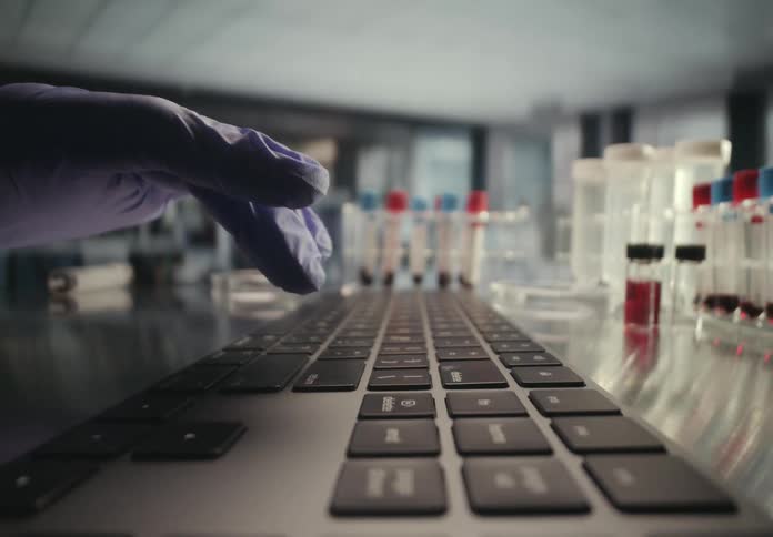 Slow motion pull back shot of a gloved hand typing on a keyboard in a scientific research laboratory with blood samples in the background