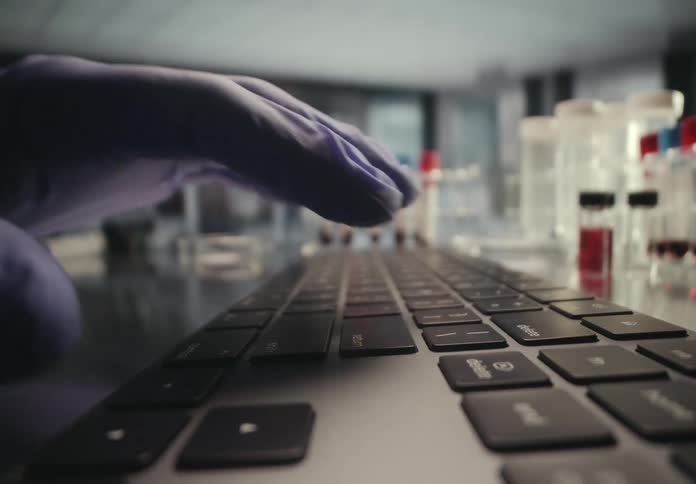 A researcher wearing gloves enters data on a computer keyboard in a modern laboratory setting